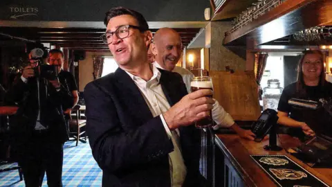 Getty Images Andy Burnham in a pub holding a pint of beer.