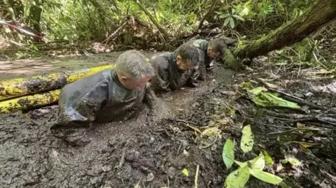 Devon and Cornwall Police Three police officers wading through mud as part of search of woodland near Desborough's cabin.