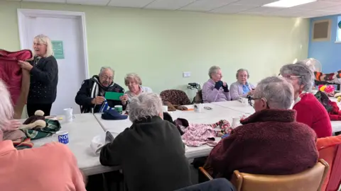 George Carden/BBC People sat around a table chatting with various nostalgic items of clothing like scarfs and gloves