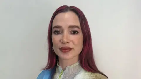 Eleanor Drage A woman with long dark red hair looks at the camera