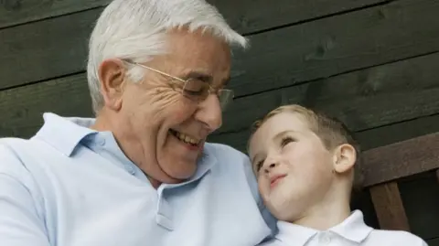 Grandfather cuddling grandson, they are smiling at each other