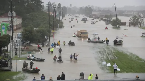 Getty Images Image shows a flooded street in Houston with rescue boats and people wading through knee-deep water.