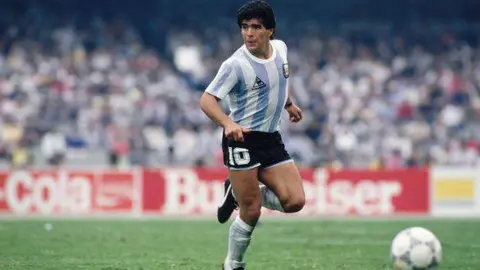 Getty Images Diego Maradona on the football pitch looks to his right as he's about to kick a ball.