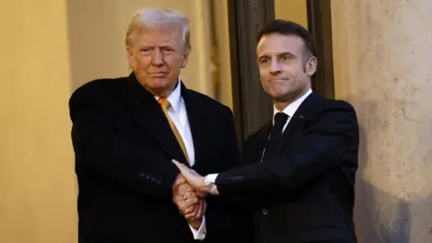 French President Emmanuel Macron welcomes US president-elect Donald J. Trump at Elysee Palace. They are gripped in a very firm handshake. Both wear dark suits 