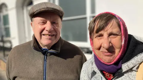 A man wearing a flat cap and a woman with a scarf round her hair