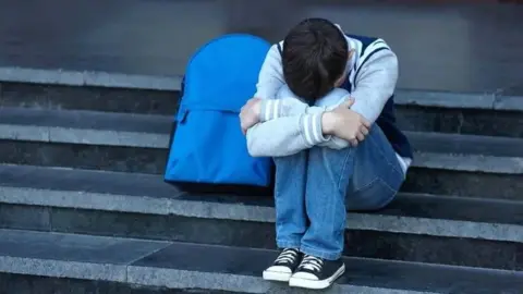 boy with schoolbag sitting on steps with his head in his arms 