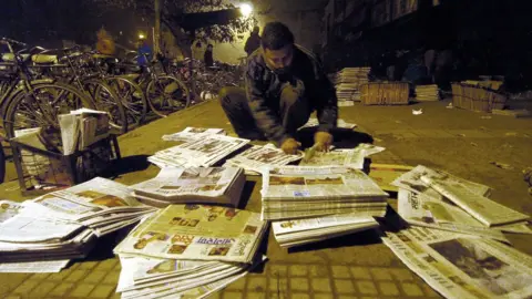 Getty Images A newspaper vendor arranging stacks of newspapers