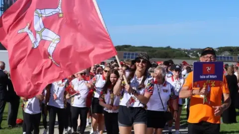 Paul Hatton Team Isle of Man headed by Laura Kinley, who is holding the Manx flag smiling.