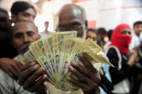 AFP An Indian man holds up old versions of the 500 rupee denomination note as people queue inside a bank to deposit 500 and 1000 Indian rupee notes in Rahimapur village on the outskirts of Allahabad on November 10, 2016