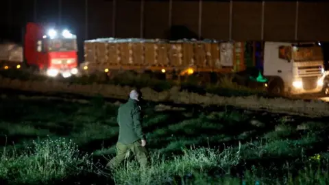 An Israeli soldier walks near aid trucks waiting by Gate 96, a newly opened entry point into Gaza