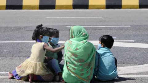 Getty Images migrant worker with children headed back home pauses for break, on day 5 of the nationwide lockdown imposed by PM Narendra Modi to check the spread of coronavirus, at Yamuna expressway zero point, on March 29, 2020 in Noida, India. (Photo by Sunil Ghosh /Hindustan Times via Getty Images)