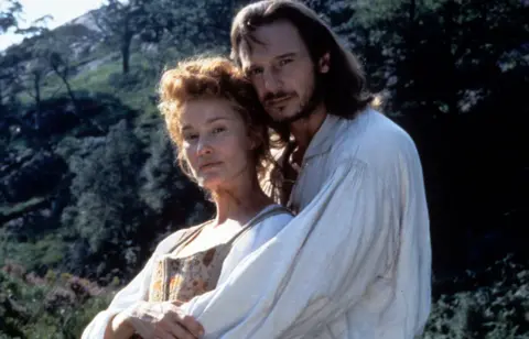 Getty Images Lange in 18th century period dress (white shirt with an embroidered dress) is being hugged by Liam Neeson, who is wearing a grubby white shirt.