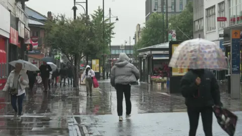 Rainy street shot of Romford town centre. People walking around with umbrellas 