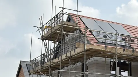 PA Media Scaffolding surrounds the roof and upper storey of a new build house. There are in-roof solar panels on the roof tiles.