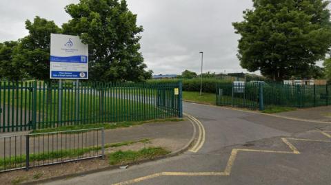 Entrance of Thomas Bewick School in Newcastle, with green fencing and a blue and white sign.