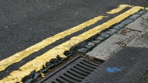 BBC A road with double yellow lines by a grate.