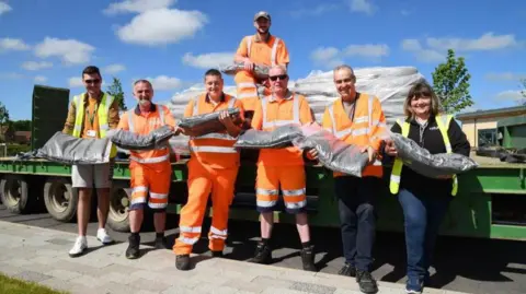East Riding of Yorkshire Council Seven people from East Riding of Yorkshire Council holding bags of compost and wearing hi-vis in front of a trailer
