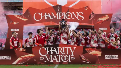 Sidemen A trophy celebration for the YouTube Allstars, with red boards with white writing reading "Champions" and "Charity match", as players celebrate.