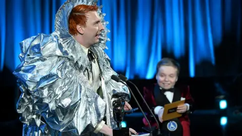 Getty Images Joe Lycett accepts the Entertainment Performance Award for 'Late Night Lycett' from Lenny Rush onstage during the 2024 BAFTA Television Awards with P&O Cruises at The Royal Festival Hall on May 12, 2024 in London, England. (