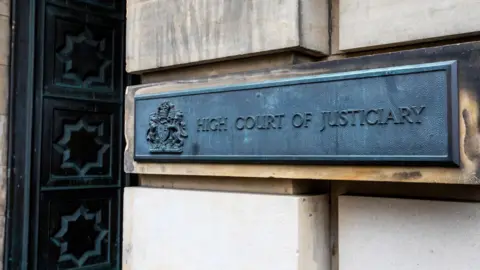 A metal sign on an exterior wall of the High Court in Edinburgh. The sign has a royal crest and the words: "High Court of Justiciary".