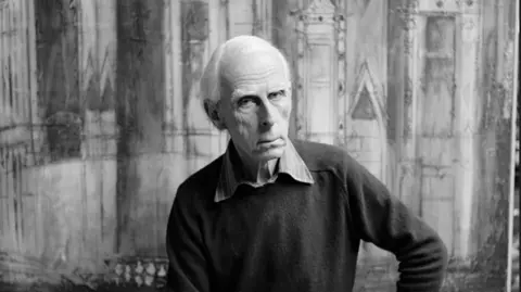 A black and white photo of a man sat in front of a painting