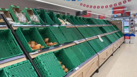 Green plastic boxes normally filled with fruit and vegetables lie almost completely empty inside the supermarket.