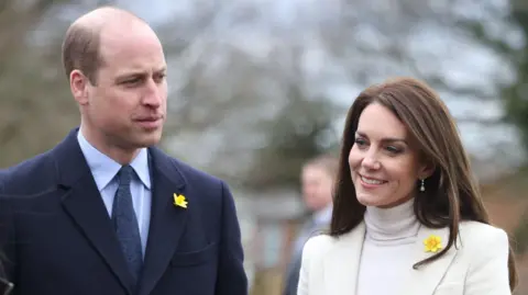 The Prince and Princess of Wales carrying out joint engagements in South Wales. Prince William is wearing a blue shirt, tie and jacket. Catherine is wearing a white polo neck and white jacket.