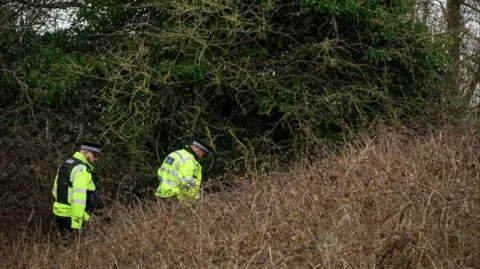 Getty Images Two uniformed police officers make their way through some woodland. Both are wearing hi-viz jackets and black hats. 