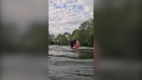 A person with short black hair swims in open water.
