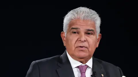 Panama's President Jose Raul Mulino - he has dark features and a full head of white hair. He is pictured here against a black backdrop, wearing a purple tie and suit