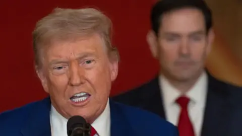Trump, who has his hair combed to the side, wears a suit as he delivers a televised addressed from the White House
