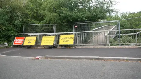 David Henwood The concrete bridge has barriers all around it to prevent people using it. There are 3 yellow signs with 'diversion' written on them and a red sign saying 'footpath closed'