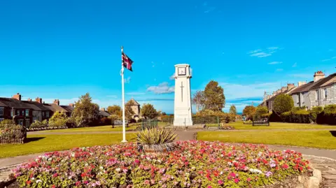 Diamond Dust A view of the war memorial in Horden park with flowers in the flowerbed and benches dotted around the grass. Terraced houses flank both sides of the park.