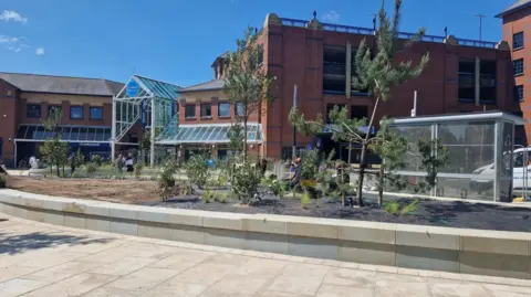 View of the renovated Riverhead Square showing flower beds edged with light coloured stones and new paving and bus shelters.