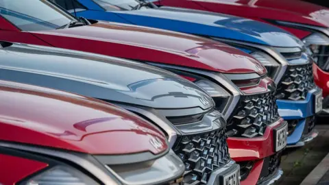 Getty Images The bonnets of five large red, blue and grey Kia cars lined up next to each other. They all have prominent grills.