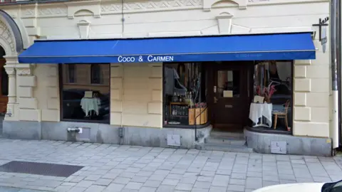 Google An exterior view of the Coco & Carmen restaurant in Stockholm, with its dark blue awning and magnolia-painted walls.