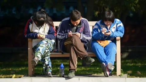 2013年11月7日、北京の公園のベンチで休憩しながら携帯電話で遊ぶ中国の若者のグループ。