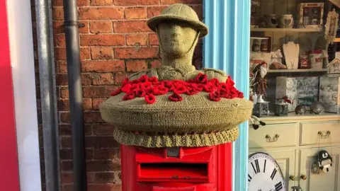 A knitted postbox topper decoration with a soldier and poppies