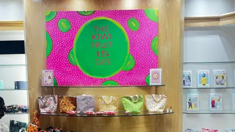 The Kiwi Fruit Is Cute A photo of a shop display with a board promoting The Kiwi Fruit Is Cute and a range of products on shelves