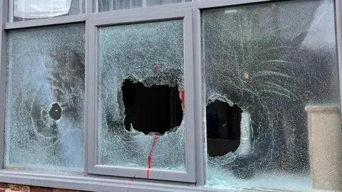 Outside of the holiday let in Old Colwyn, where three windows are smashed through. Traces of red paint can be seen on the pavement.