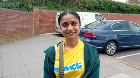 A young woman in a yellow shirt and green jumper smiles at the camera.