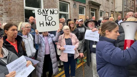 Protesters hold signs up outside while stood on the road outside the Crispin Arms