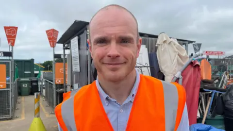 Simon is standing next to a container of items that are being disposed of at a household and waste recycling centre
