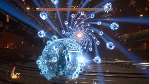 Sony/Housemarque Gameplay screenshot from Saros shows a screen filled with spherical blue projectiles hurtling towards the player character, who is surrounded by a blue shield sphere as he runs towards the deluge. The character's health bar is visible in the left corner and at the top of the screen a three-part boss health bar labelled "Bastion" is visible.