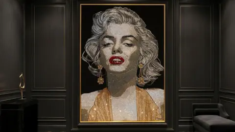 A portrait of Marilyn Monroe made out of crystals. She is wearing a gold top with red lipstick.