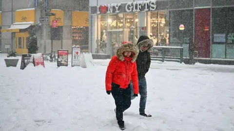Two people, dressed in thick coats, walk through the snow in New York City