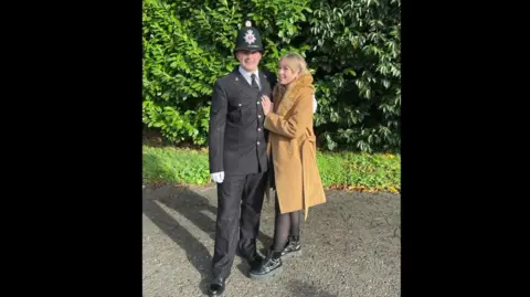 Supplied A man in police uniform stands with a blonde woman in a long brown coat. 