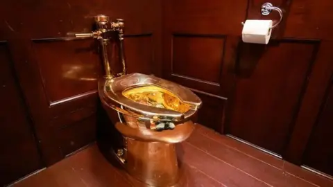 Getty Images The golden toilet sitting in a corner of a room panelled with dark wood.