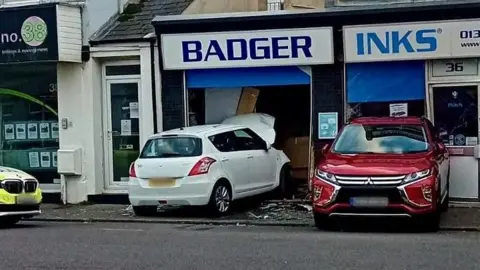 A white car has crashed through the window of a shop.
