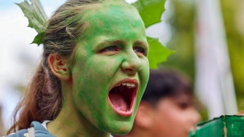 Headshot of a demonstrator with her face painted green at a climate rally
